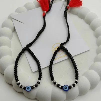 Sophisticated Texture for Sacred Protection. Elevate your baby's daily wardrobe with the KJJ Elite Baby Nazariya, where artistic detail meets traditional shielding. This premium set features a striking central blue evil eye charm flanked by unique 2.5mm imported silver balls with a corrugated (ridged) texture. The fine vertical lines on these silver beads catch the light with every tiny movement, providing a rich, multi-dimensional sparkle that sets this piece apart from standard smooth-bead designs. Handcrafted with certified 92.5 Sterling Silver, these bracelets are meticulously hand-strung on a soft, durable black cord with polished black beads to ward off negative energy. Designed to be as gentle as it is beautiful, this set ensures your little one stays protected with the highest quality materials and a touch of modern luxury. Key Highlights: Unique Corrugated Silver Texture: Features premium 2.5mm imported silver balls with a distinctive ridged pattern for an upscale and light-catching finish. Certified 92.5 Sterling Purity: Every silver bead is made from guaranteed high-purity silver, ensuring a hypoallergenic and long-lasting shine that is safe for infants. Sacred Evil Eye Protection: Adorned with a vibrant blue evil eye charm at the center, traditionally used to shield children from the "evil eye" and bring good fortune. Adjustable Artisan Cord: Fitted on a soft black thread with our signature red and black tassel, providing a secure and custom fit as your baby grows. A Gift of Devotion and Quality: The perfect choice for "Namkaran" ceremonies, first birthdays, or as a meaningful homecoming blessing for a newborn. Product Specifications: Brand: Kanhaji Jewels (KJJ) Material: 92.5 Sterling Silver & High-Grade Protective Beads Silver Ball Texture: 2.5mm Corrugated / Ridged (Imported) Category: Infant Protection Jewelry / Nazariya Quantity: 1 Pair (Set of 2)