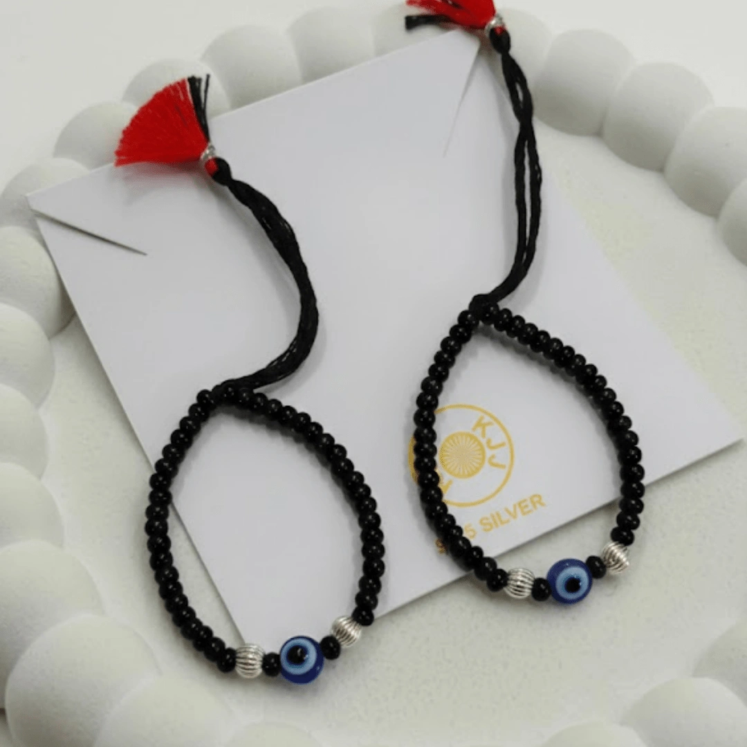 Sophisticated Texture for Sacred Protection. Elevate your baby's daily wardrobe with the KJJ Elite Baby Nazariya, where artistic detail meets traditional shielding. This premium set features a striking central blue evil eye charm flanked by unique 2.5mm imported silver balls with a corrugated (ridged) texture. The fine vertical lines on these silver beads catch the light with every tiny movement, providing a rich, multi-dimensional sparkle that sets this piece apart from standard smooth-bead designs. Handcrafted with certified 92.5 Sterling Silver, these bracelets are meticulously hand-strung on a soft, durable black cord with polished black beads to ward off negative energy. Designed to be as gentle as it is beautiful, this set ensures your little one stays protected with the highest quality materials and a touch of modern luxury. Key Highlights: Unique Corrugated Silver Texture: Features premium 2.5mm imported silver balls with a distinctive ridged pattern for an upscale and light-catching finish. Certified 92.5 Sterling Purity: Every silver bead is made from guaranteed high-purity silver, ensuring a hypoallergenic and long-lasting shine that is safe for infants. Sacred Evil Eye Protection: Adorned with a vibrant blue evil eye charm at the center, traditionally used to shield children from the "evil eye" and bring good fortune. Adjustable Artisan Cord: Fitted on a soft black thread with our signature red and black tassel, providing a secure and custom fit as your baby grows. A Gift of Devotion and Quality: The perfect choice for "Namkaran" ceremonies, first birthdays, or as a meaningful homecoming blessing for a newborn. Product Specifications: Brand: Kanhaji Jewels (KJJ) Material: 92.5 Sterling Silver & High-Grade Protective Beads Silver Ball Texture: 2.5mm Corrugated / Ridged (Imported) Category: Infant Protection Jewelry / Nazariya Quantity: 1 Pair (Set of 2)